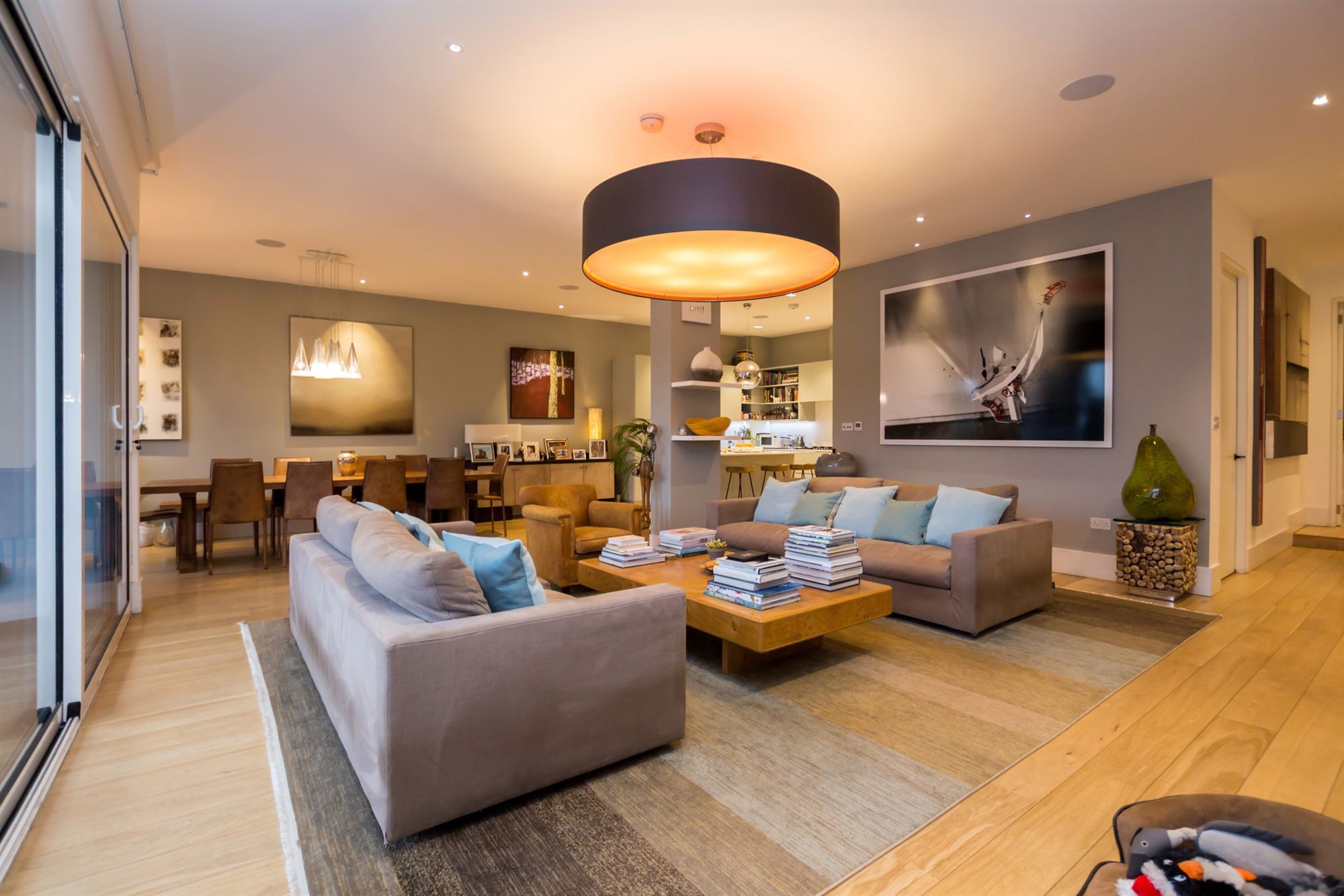 An open-plan living and dining room lit with a large drum pendant, recessed downlights and picture lighting