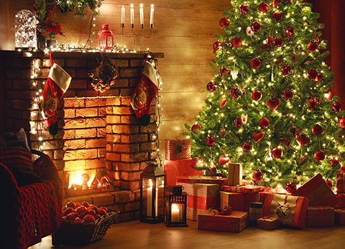A Christmas tree lit with warm white fairy lights beside a fireplace
