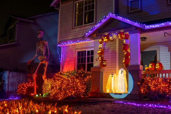 A house decorated for Halloween with purple roofline lights, orange-lit hedges, glowing ghosts and jack-o'-lanterns