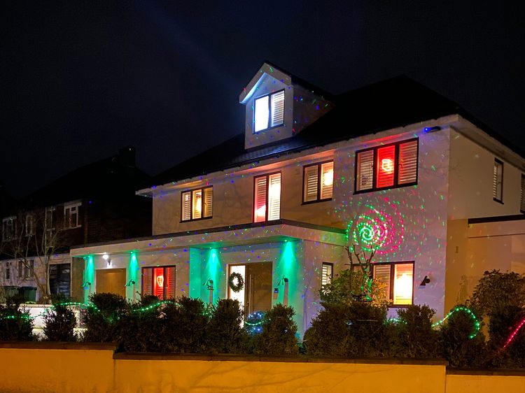 A house at night lit in green and red with a projector on the front